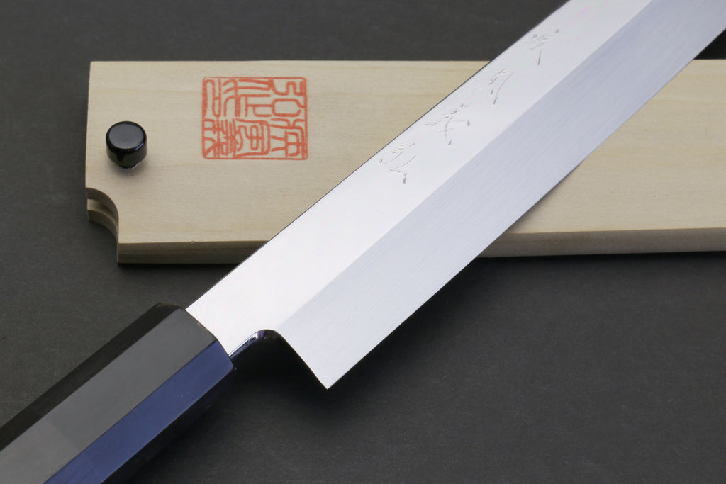 Japanese chef knife with mirror-finished blade, dark bolster, and ebony handle.