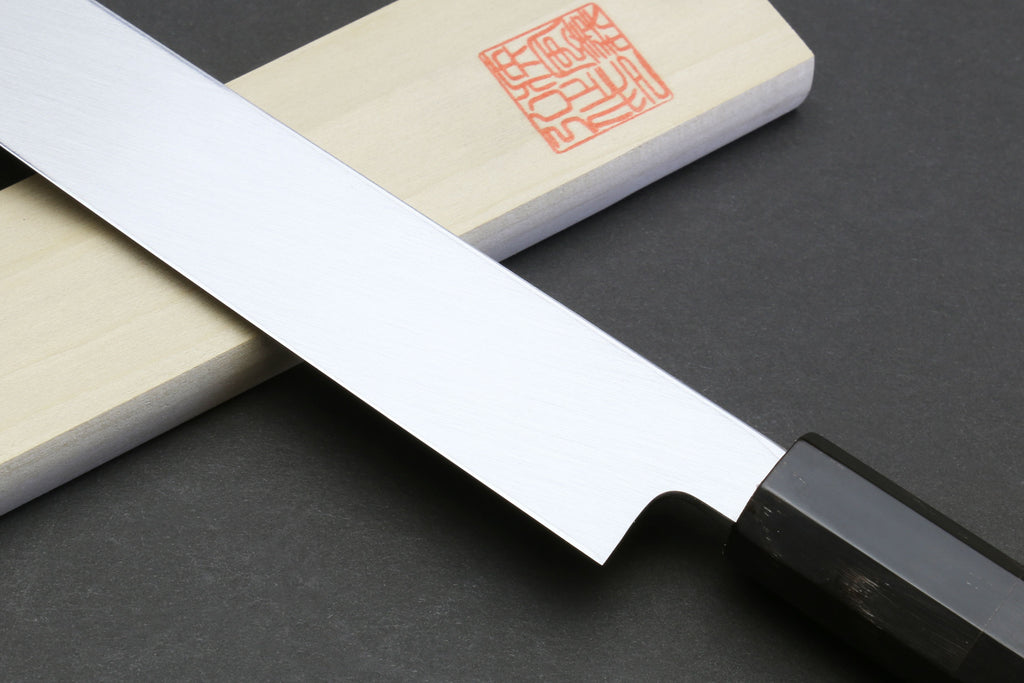 Mirror-finished sushi knife blade edge with dark handle and bolster.