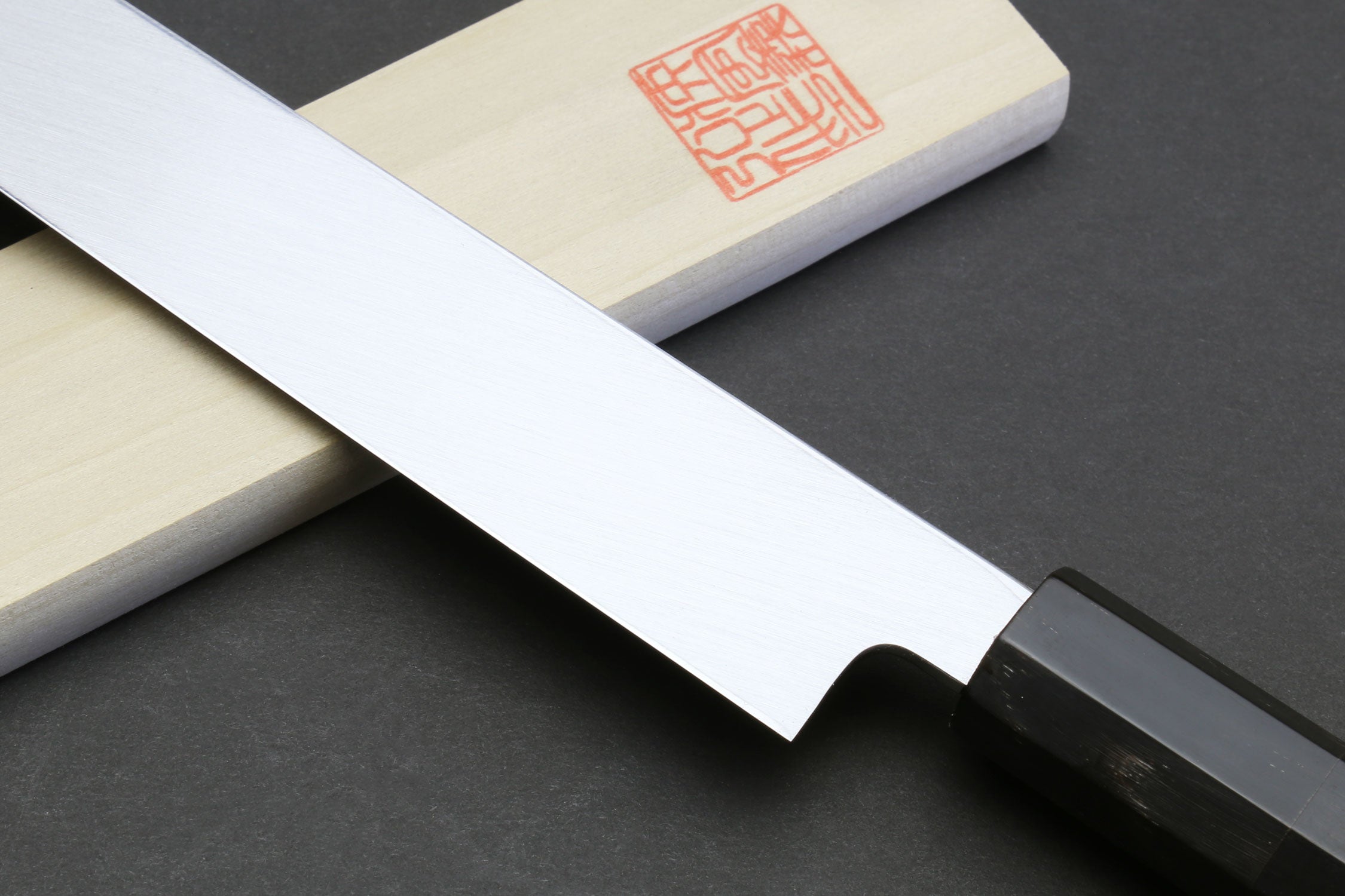 Mirror-finished sushi knife blade edge with dark handle and bolster.