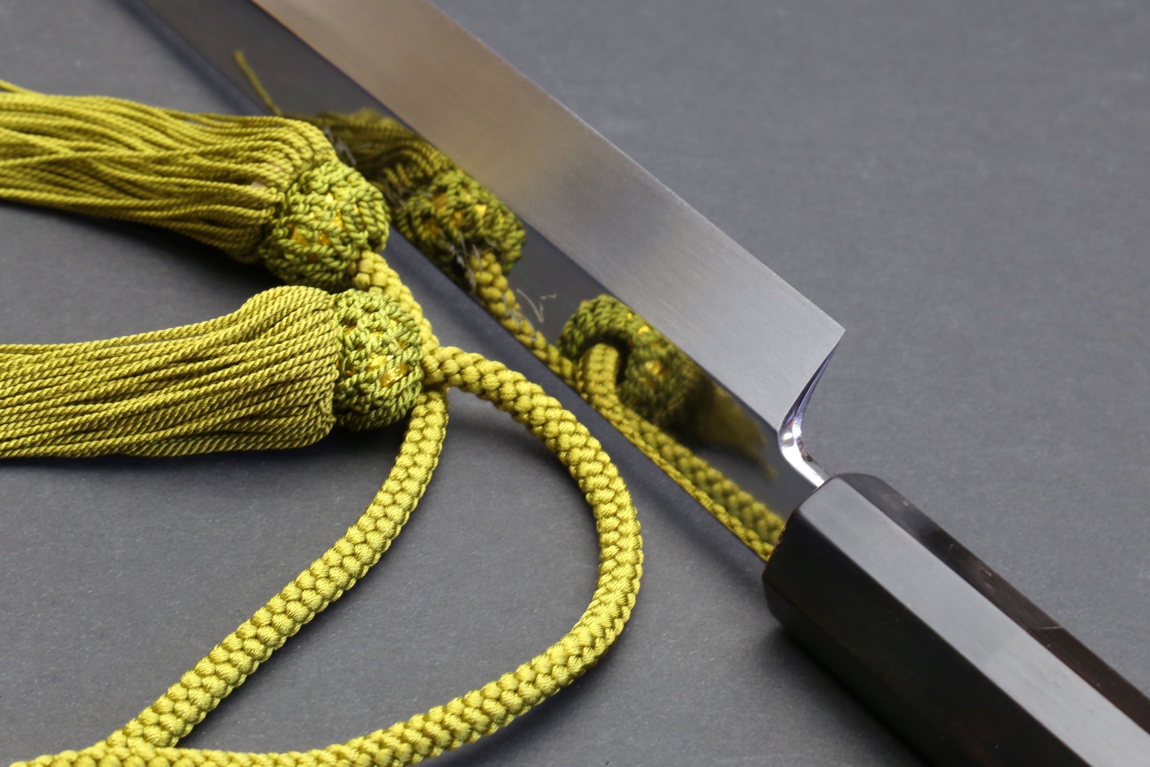 Mirror-finished chef knife blade with pointed tip and dark ebony handle, cord tied.