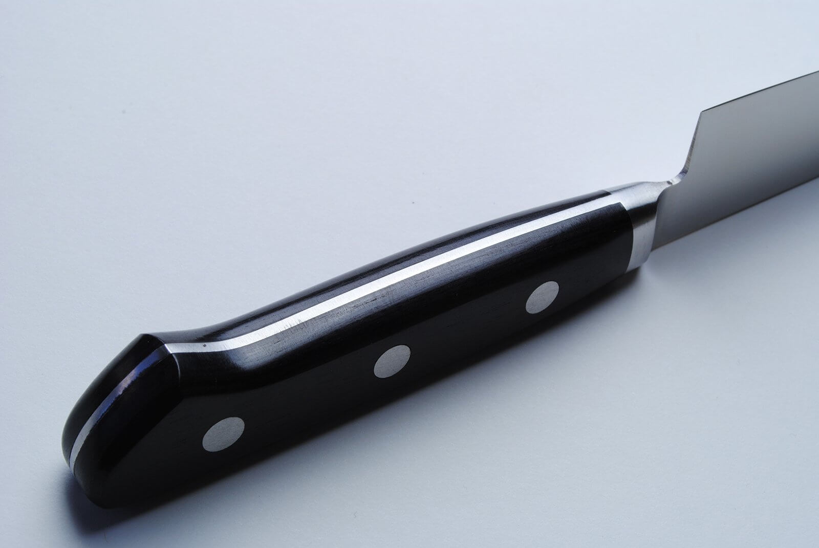 Stain-resistant gyuto knife close-up: glossy black handle with rivets