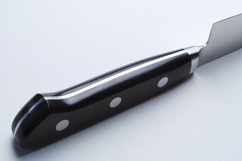 Santoku chef’s knife handle close-up with black scales and silver rivets on dark bolster
