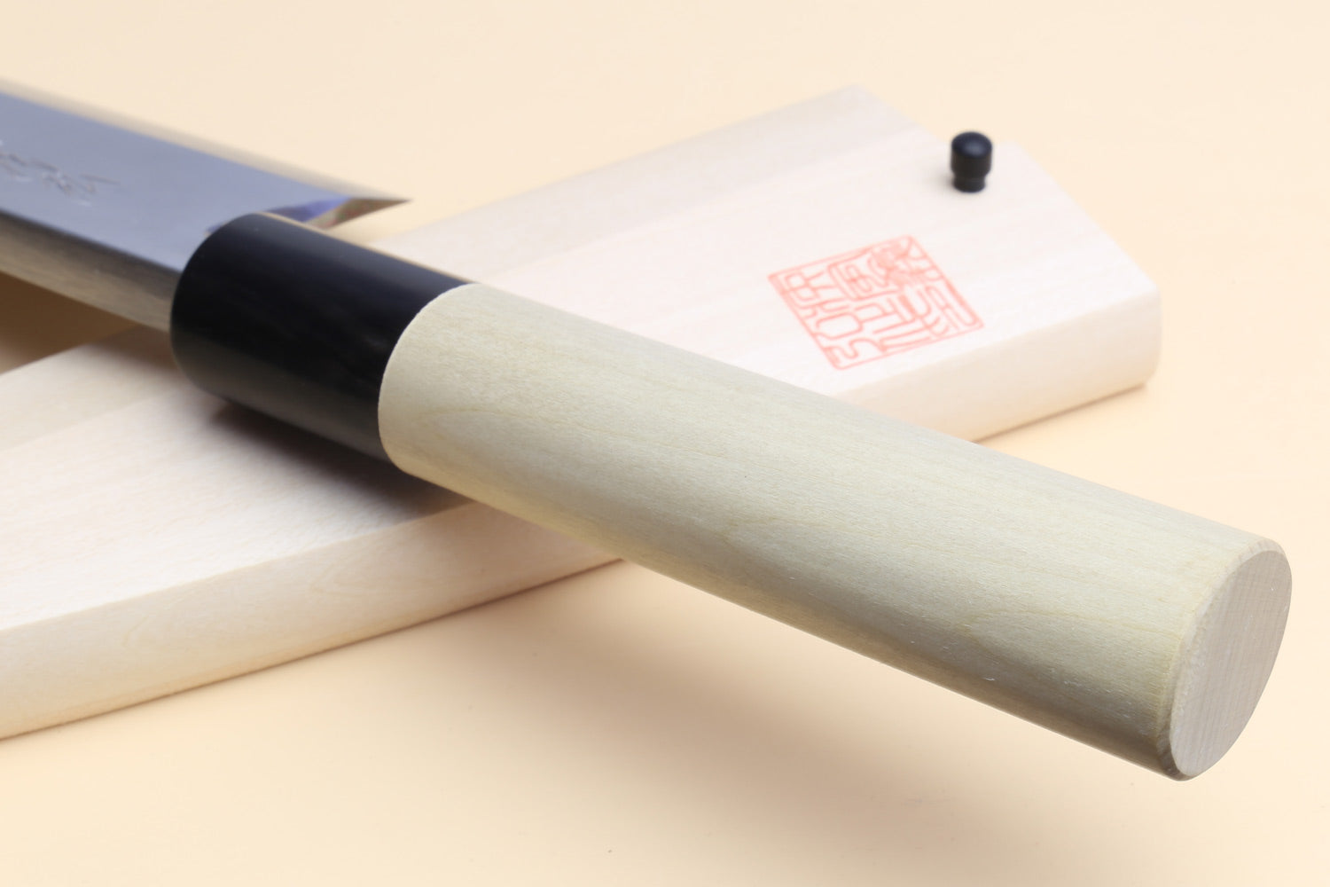 Deba knife angled view: white blade, magnolia handle, black grip collar and pin