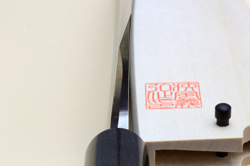 Deba knife close-up: white blade edge, black ferrule, light magnolia handle