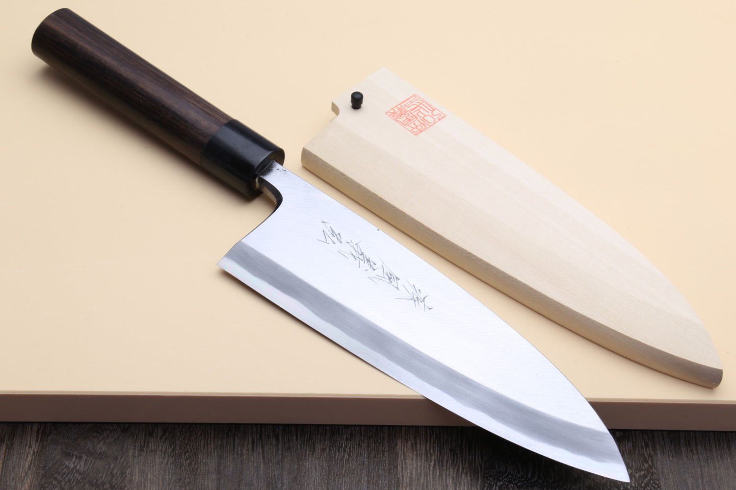 Deba fish fillet knife with white blade and dark rosewood handle, angled on surface