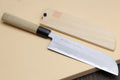 Japanese vegetable chef knife with dark blade and light wood handle, with matching sheath.