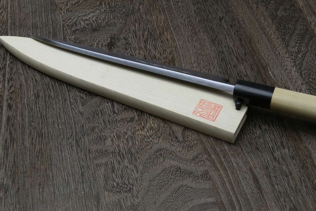 Sashimi filet knife with silver blade resting in light wood saya, black bolster