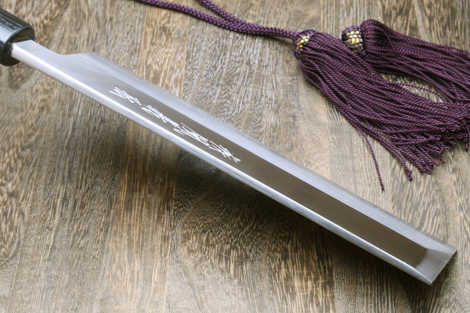 White steel knife with engraved lettering and purple cord tied; dark handle