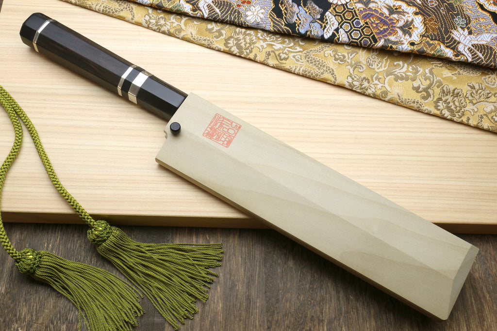 Japanese vegetable knife with dark handle and silver rings, in light wooden saya