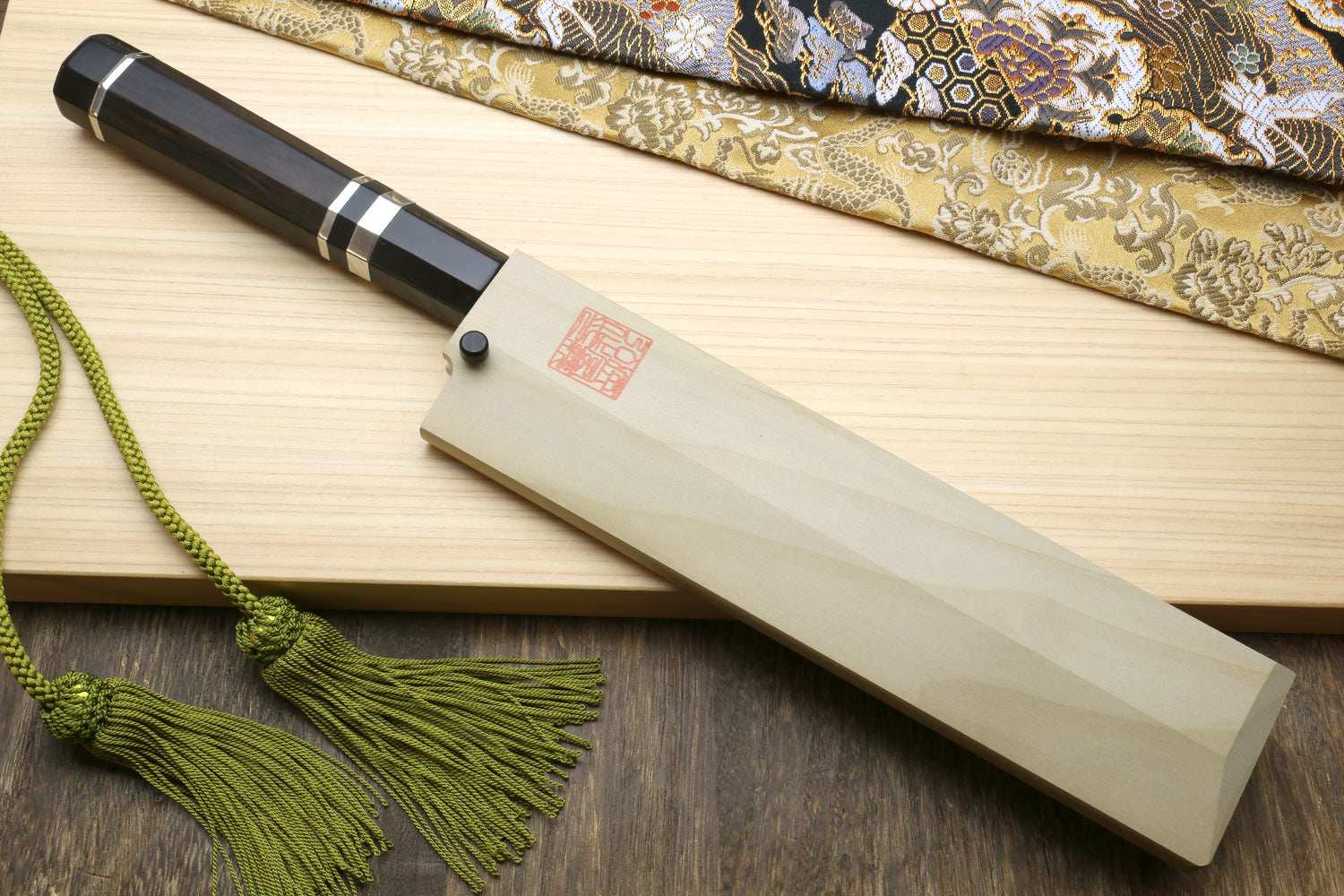 Japanese vegetable knife with dark handle and silver rings, in light wooden saya