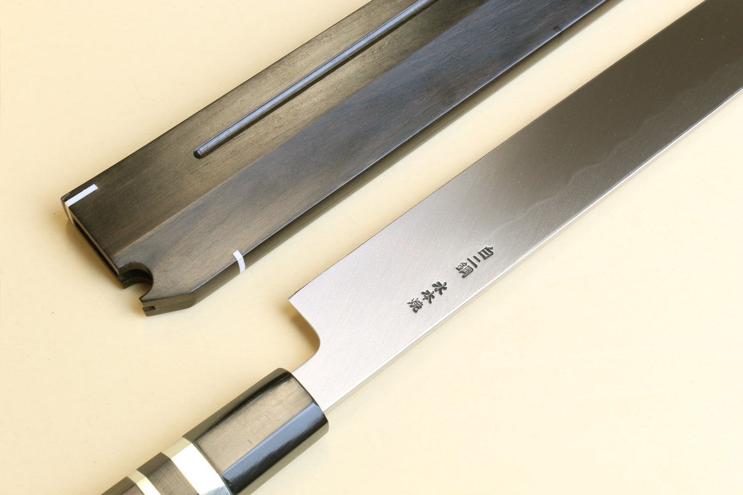 Yanagi sushi knife with silver steel blade, dark handle, and wooden saya