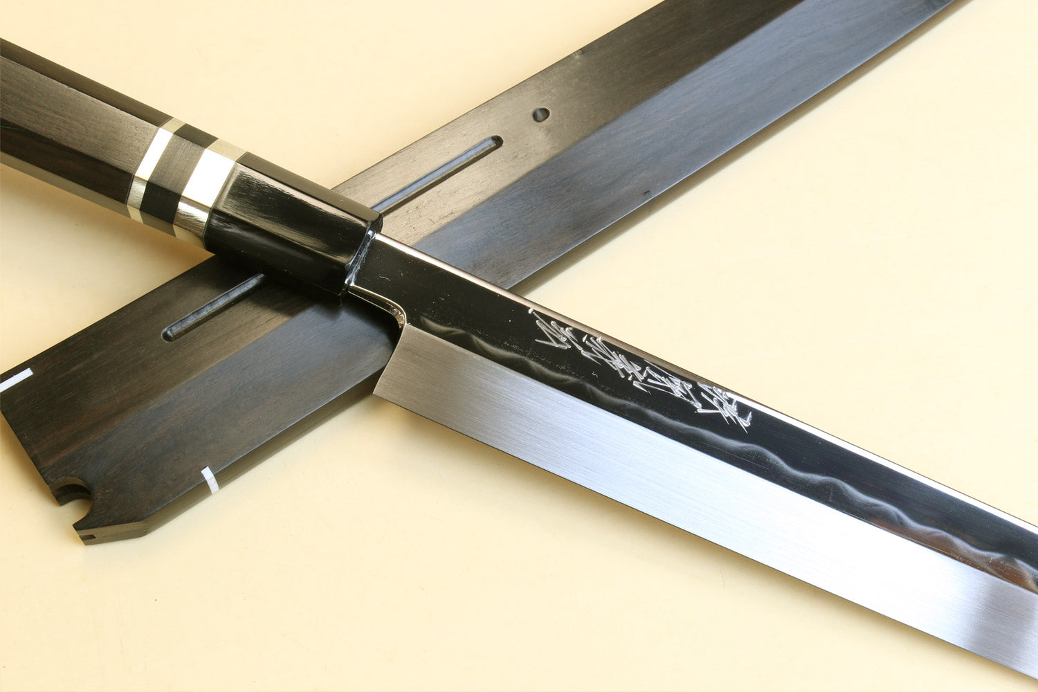 Japanese yanagi knife with mirror-finished steel blade, dark wood handle, and saya
