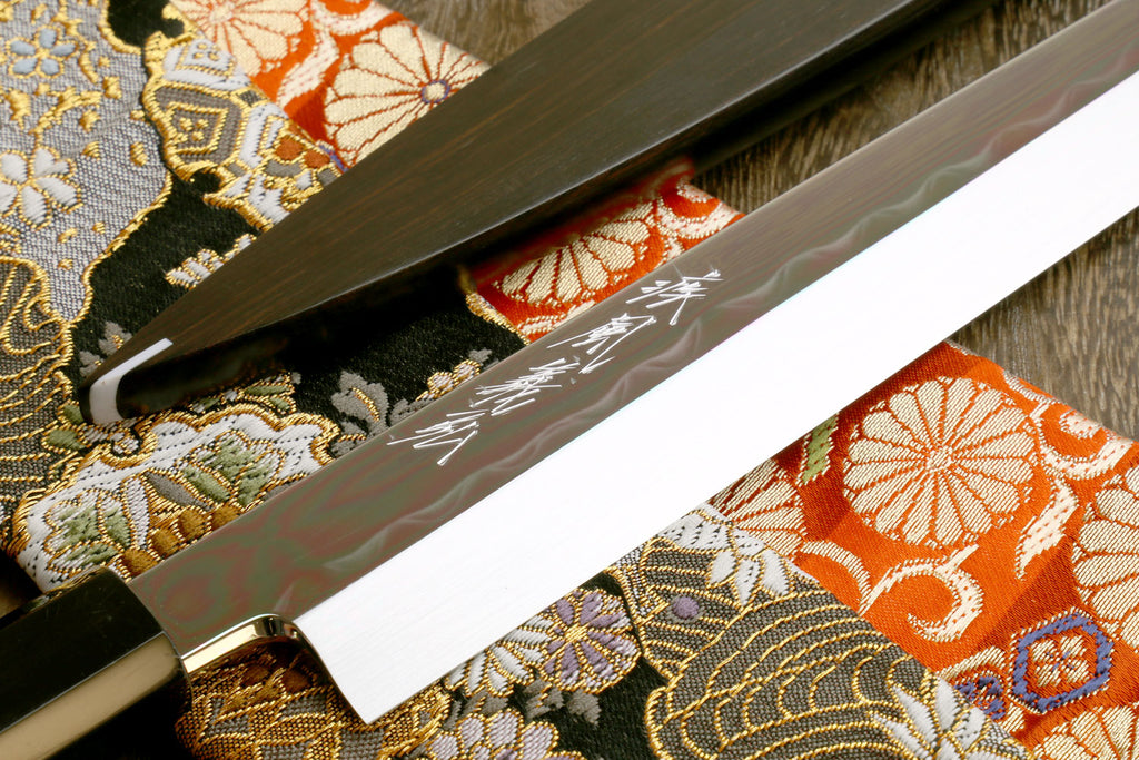 Sashimi knife blade close-up on patterned fabric, mirror-finished steel with etched marks