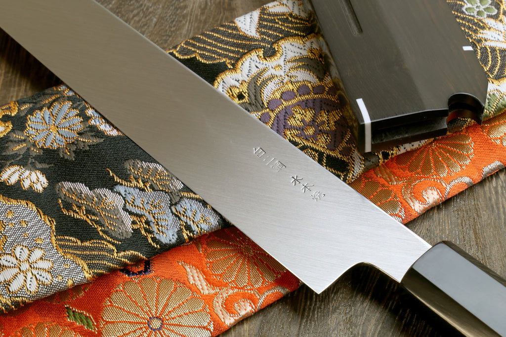 Sashimi knife in saya with mirror-finished steel blade, ebony handle, on patterned cloth