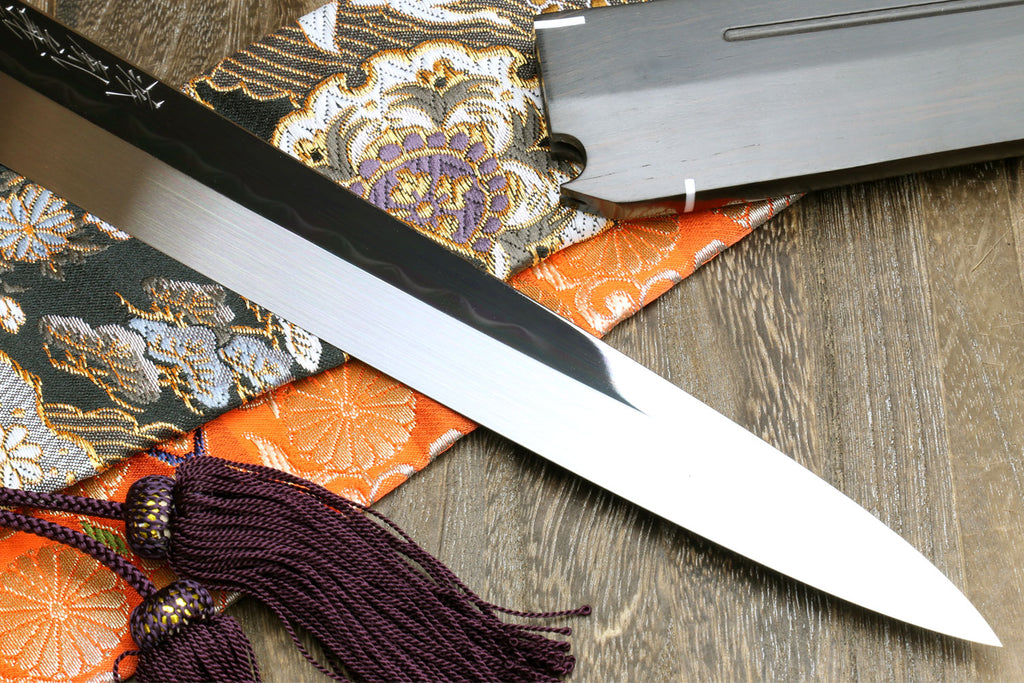 Sashimi knife with mirror-finished blade and saya, purple cord tassel on patterned fabric