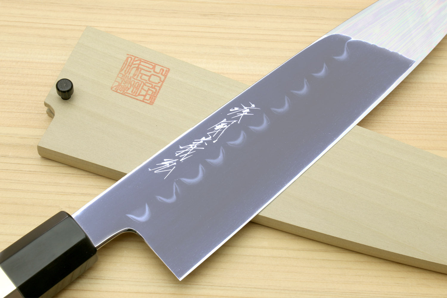 Japanese chef knife with wavy engraved blade, dark handle, and silver ring