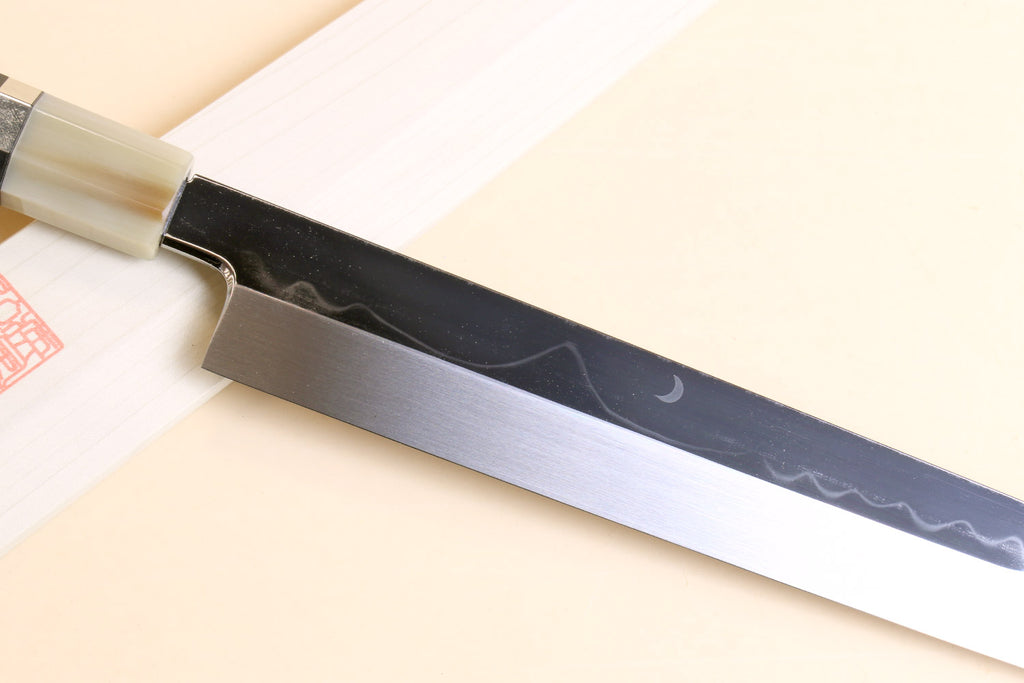 Japanese kitchen knife with dark patterned blade and pale wood handle