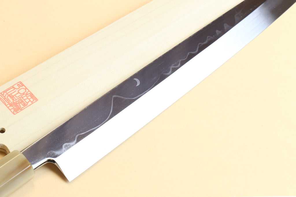 Japanese kitchen knife showing long patterned steel blade and pale wood handle