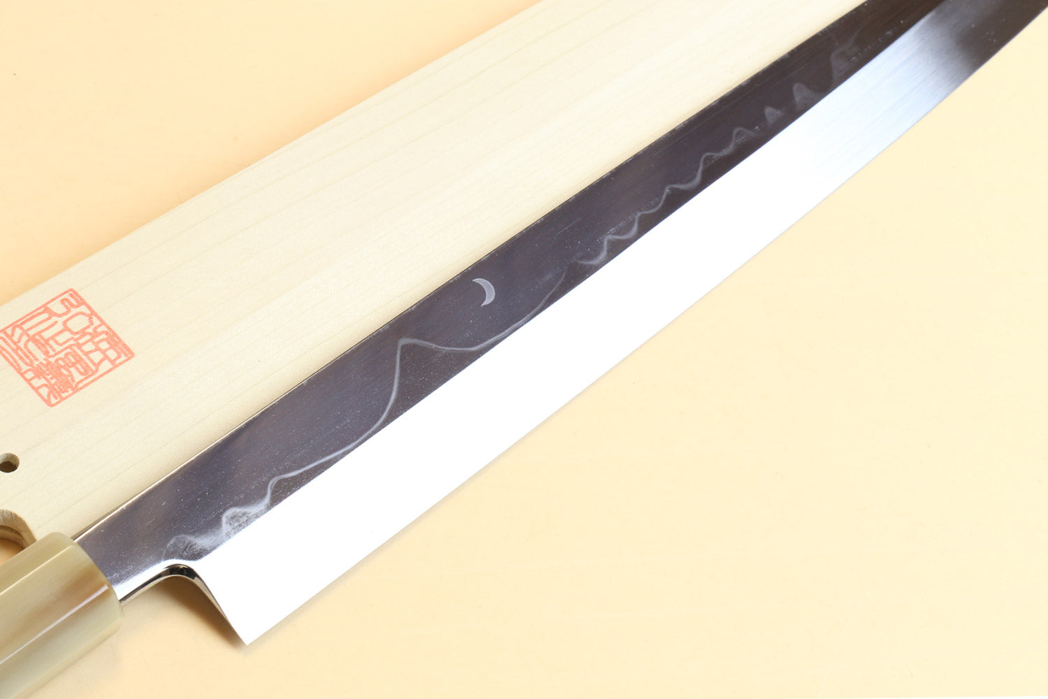 Japanese kitchen knife showing long patterned steel blade and pale wood handle