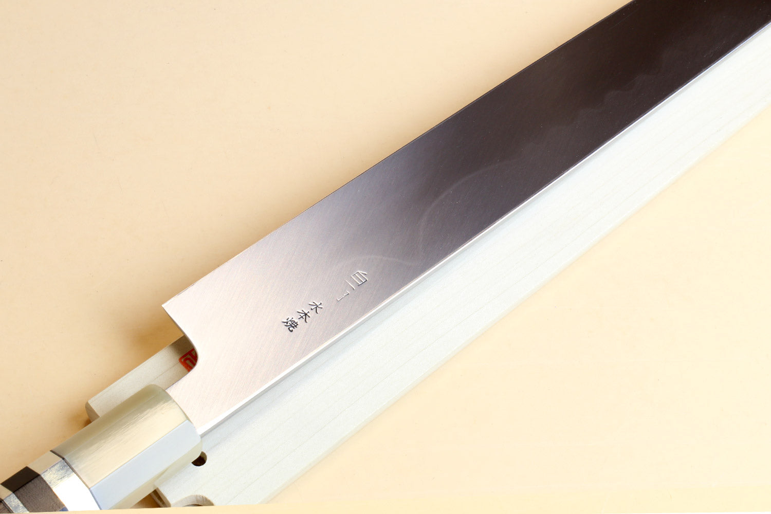 Japanese kitchen knife with mirror-bright blade edge and pale wood handle