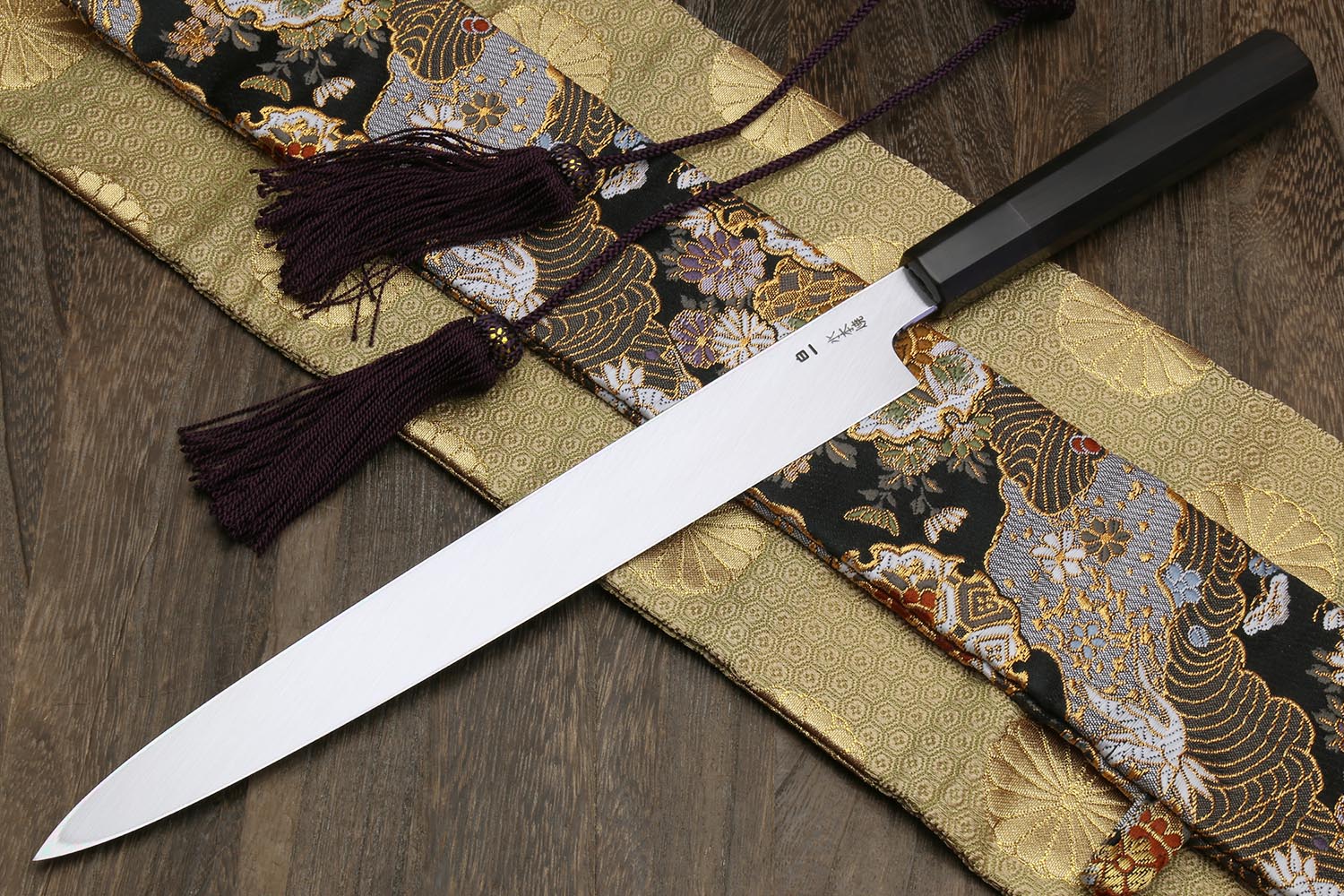 Yanagi knife with white steel blade and dark handle on gold and black patterned cloth