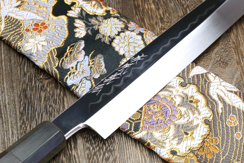 Yanagi knife blade close-up with mirror edge on gold and black patterned fabric