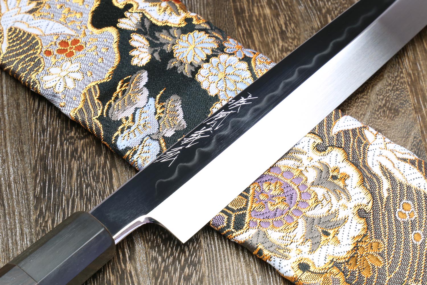 Yanagi knife blade close-up with mirror edge on gold and black patterned fabric