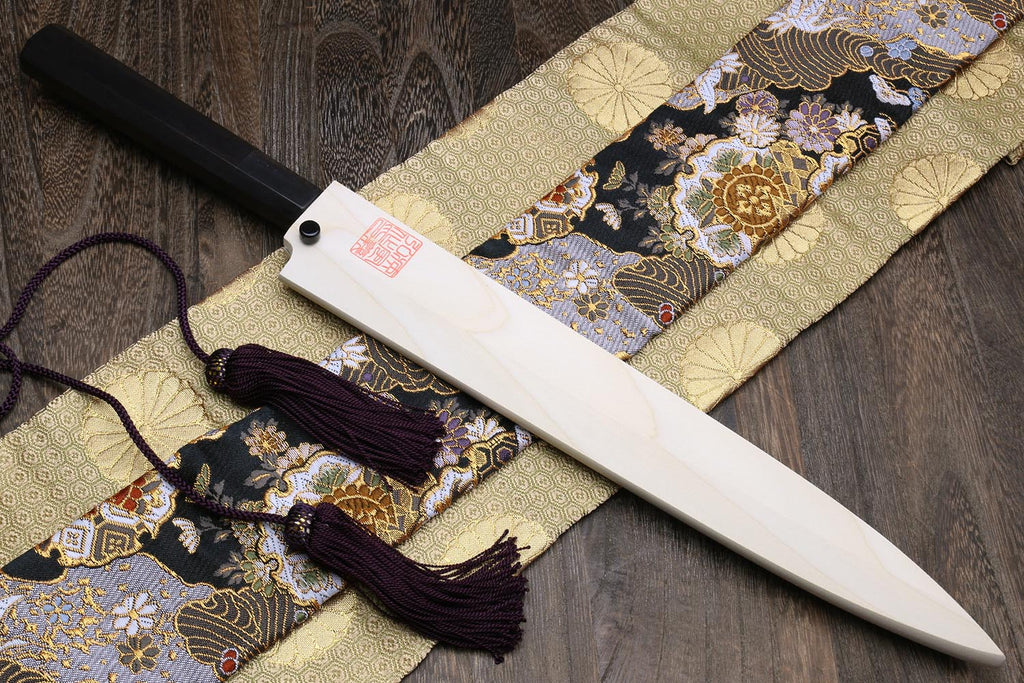 Yanagi knife with white steel blade and dark handle on patterned cloth with tassels