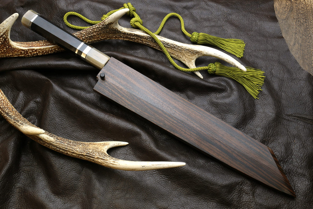 Kiritsuke knife with dark handle, horn sheath, and green cord tassel.