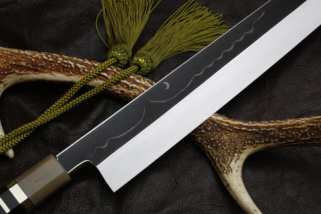 Engraved Kiritsuke knife blade with ivory-and-horn handle and green tassel cord.
