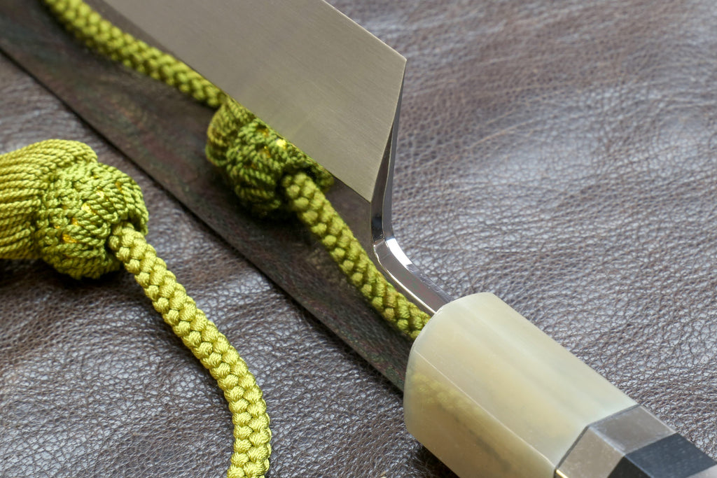 Knife handle close-up with ivory wrap and silver-toned bands, green cord.