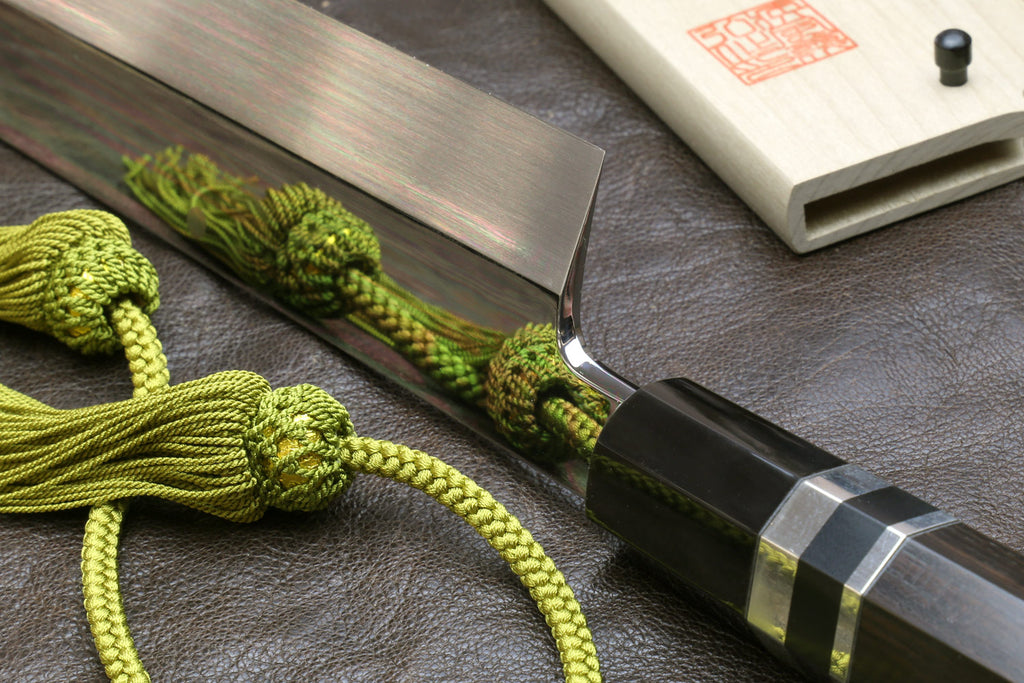 Japanese-style kitchen knife with wavy steel blade beside light wood sheath