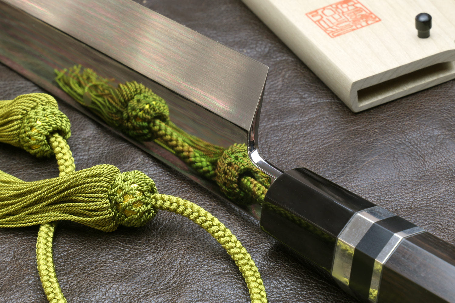 Japanese-style kitchen knife with wavy steel blade beside light wood sheath