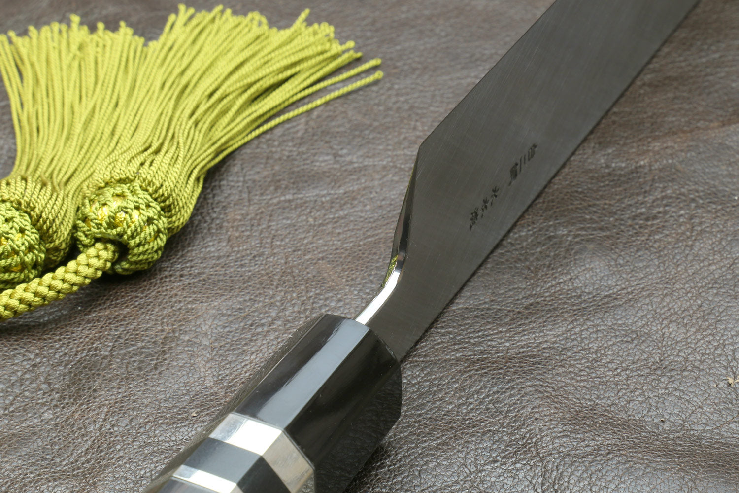 Japanese-style kitchen knife blade with green tassel cord and light wood sheath