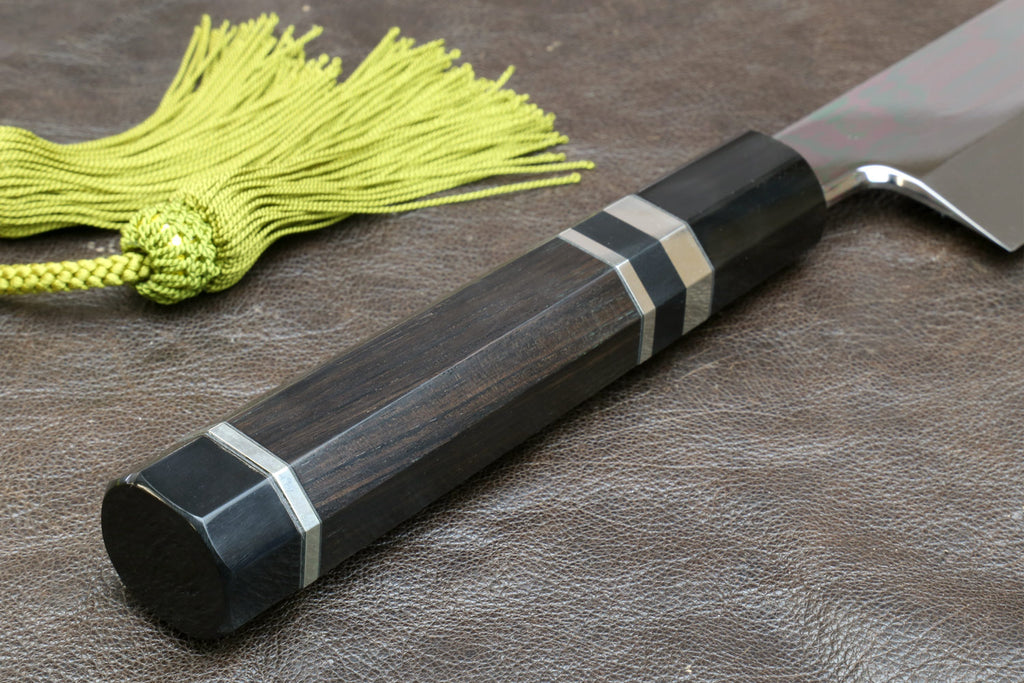 Japanese-style kitchen knife with dark handle and wavy steel blade, green tassel cord