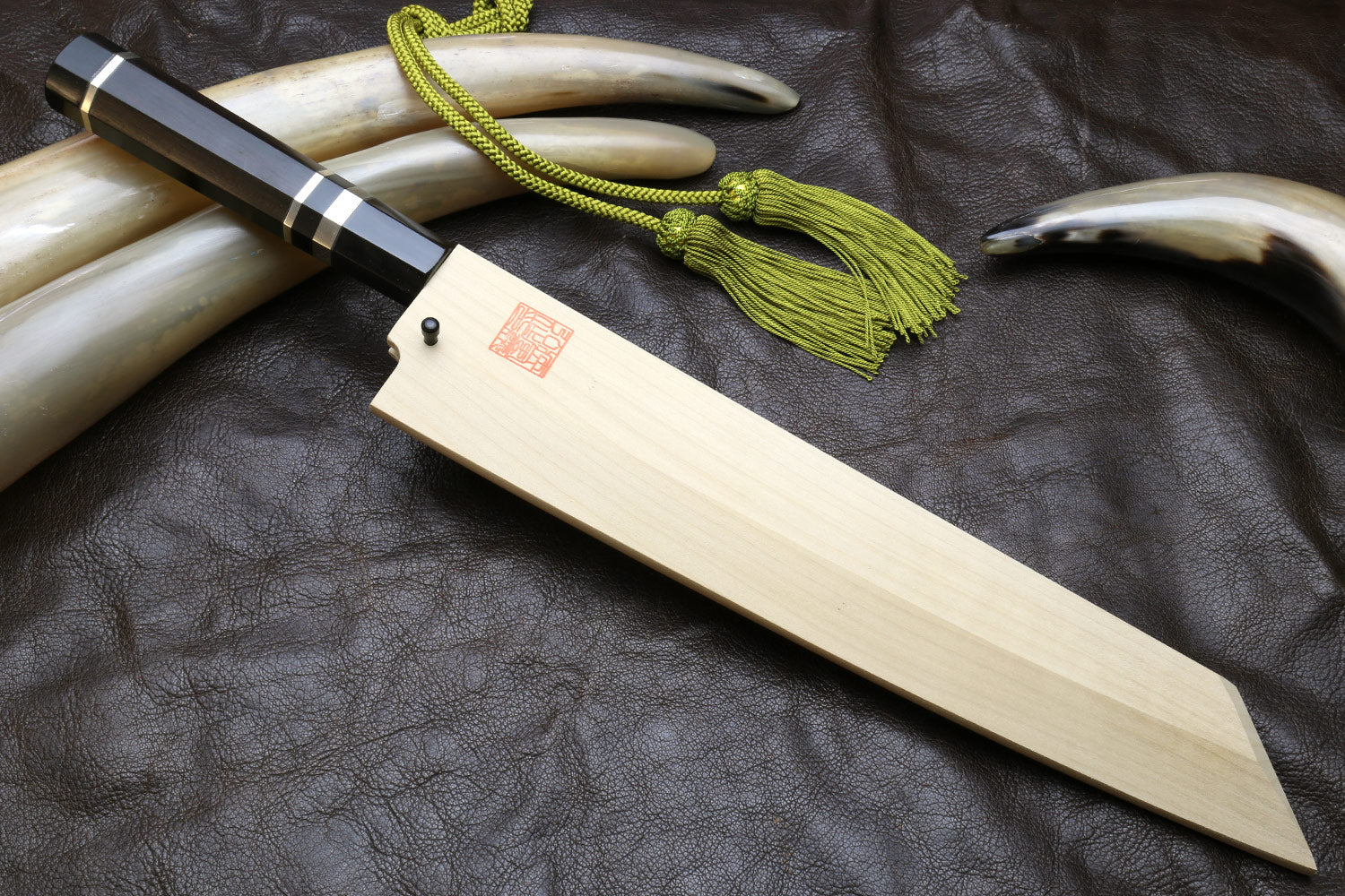 Japanese-style kitchen knife with wavy steel blade and light wood sheath, green cord tassel