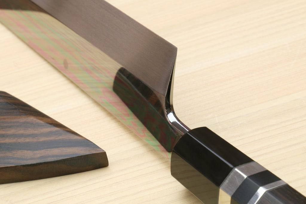Kiritsuke chef knife handle end with dark saya sheath on light wood