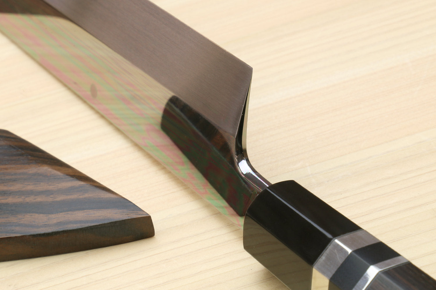 Kiritsuke chef knife handle end with dark saya sheath on light wood