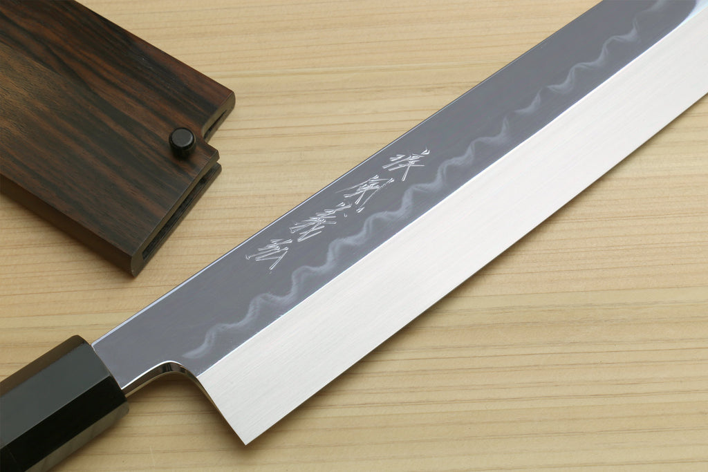 Japanese kitchen knife blade close-up with wavy hamon and etched text