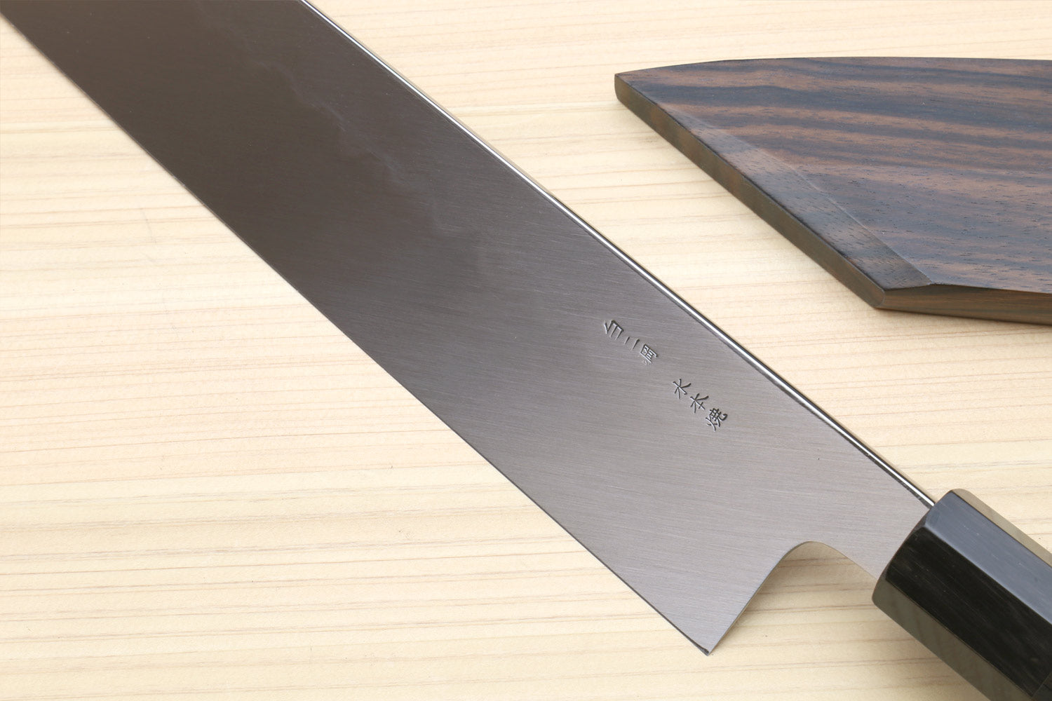 Japanese kitchen knife blade with etched markings and dark handle