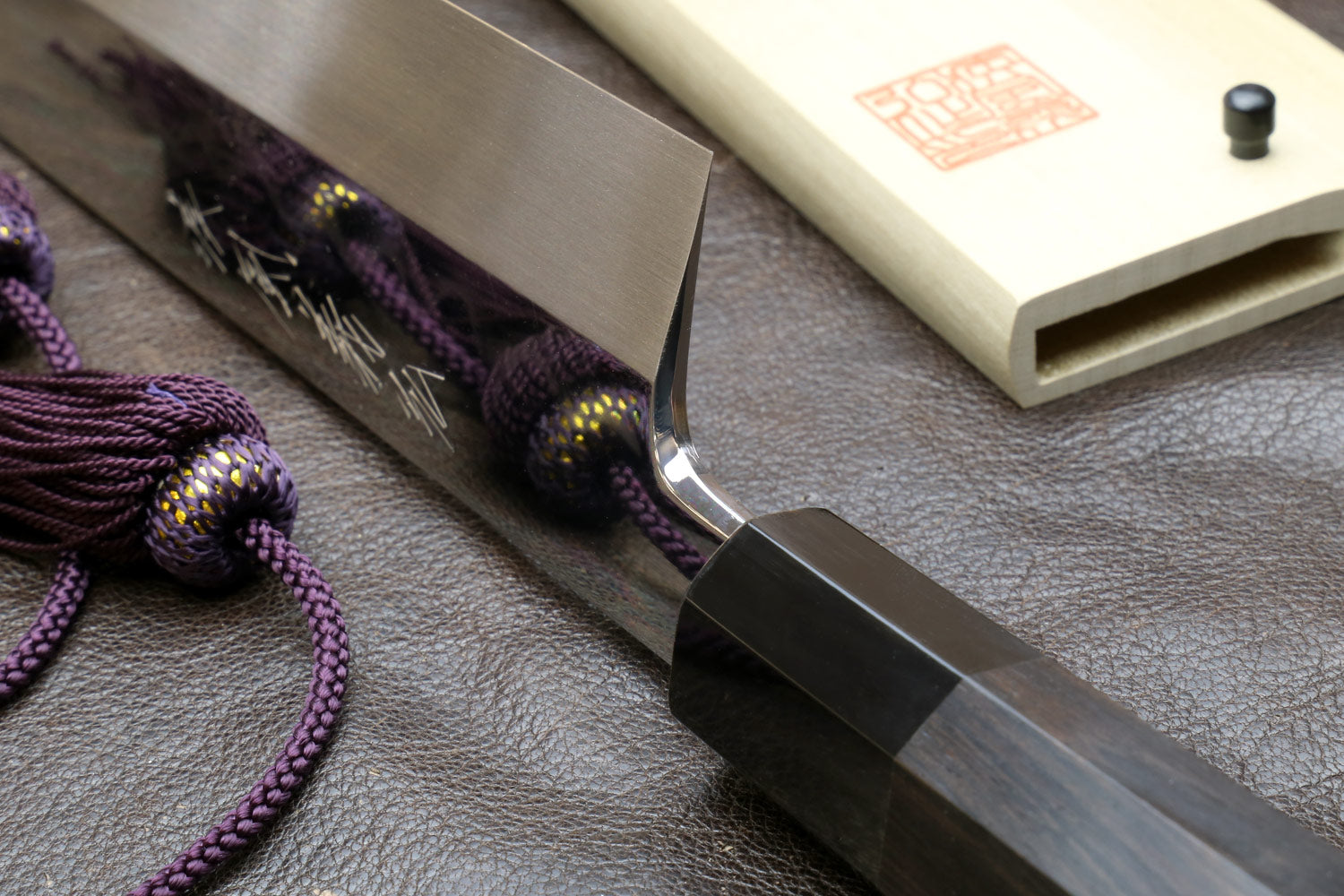 Kiritsuke knife and saya with dark handle; mirror-polished blade near the sheath