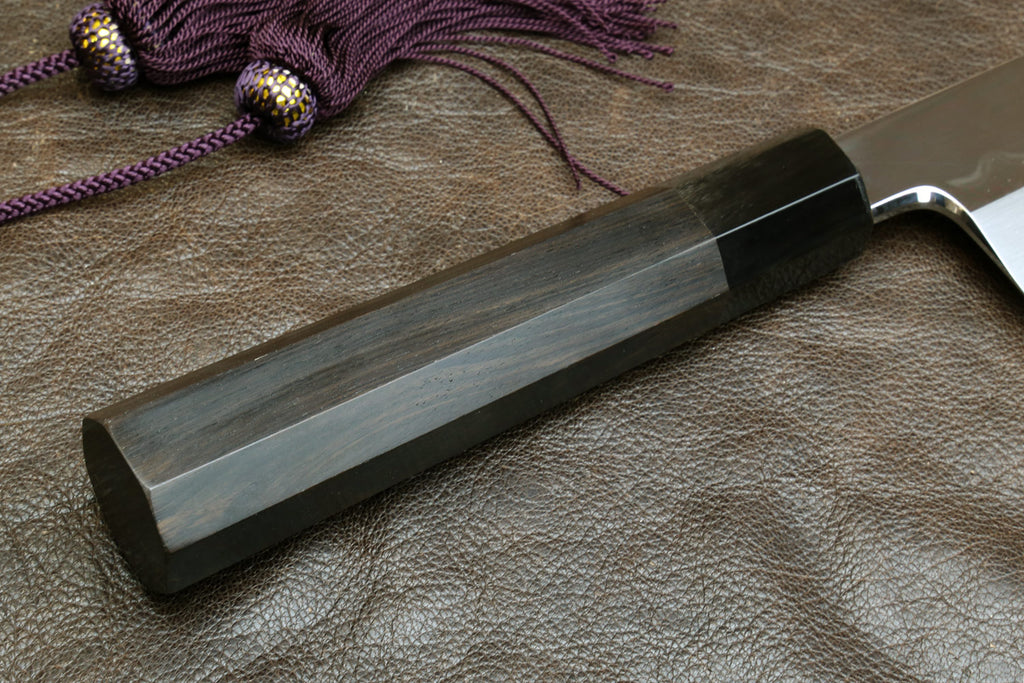Kiritsuke knife with dark handle and mirror-polished steel blade, side view