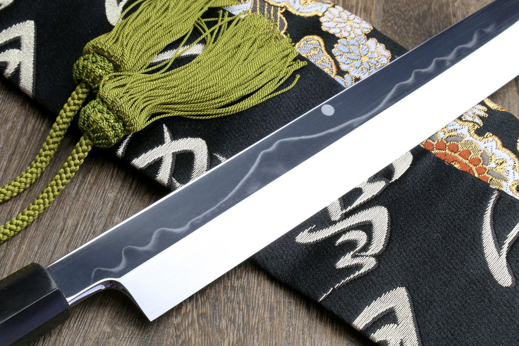 Mirror-finished Japanese kitchen knife with dark handle and patterned cloth sheath roll