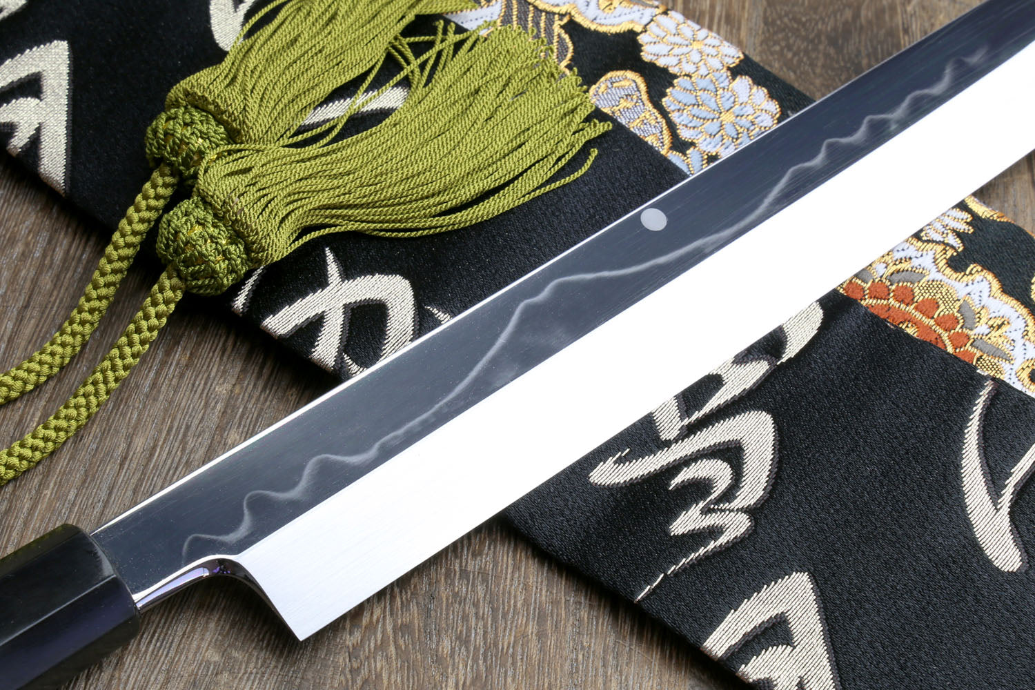 Mirror-finished Japanese kitchen knife with dark handle and patterned cloth sheath roll