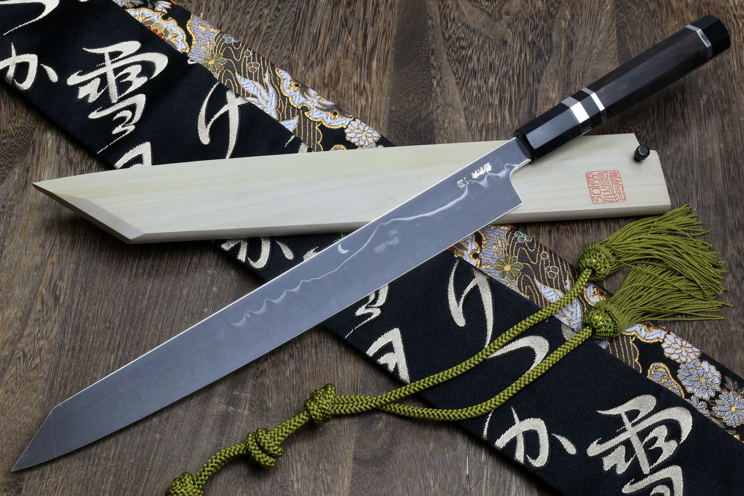 Japanese kiritsuke-style knife with mirror-finished blade, dark handle, and cloth wrap