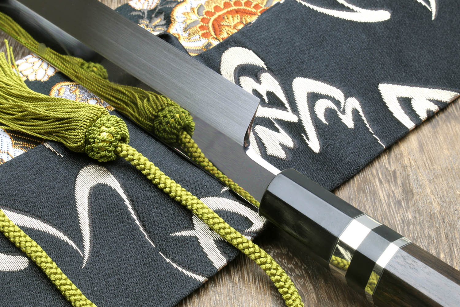 Japanese kitchen knife with mirror-finished blade, dark handle, and green cord tassel