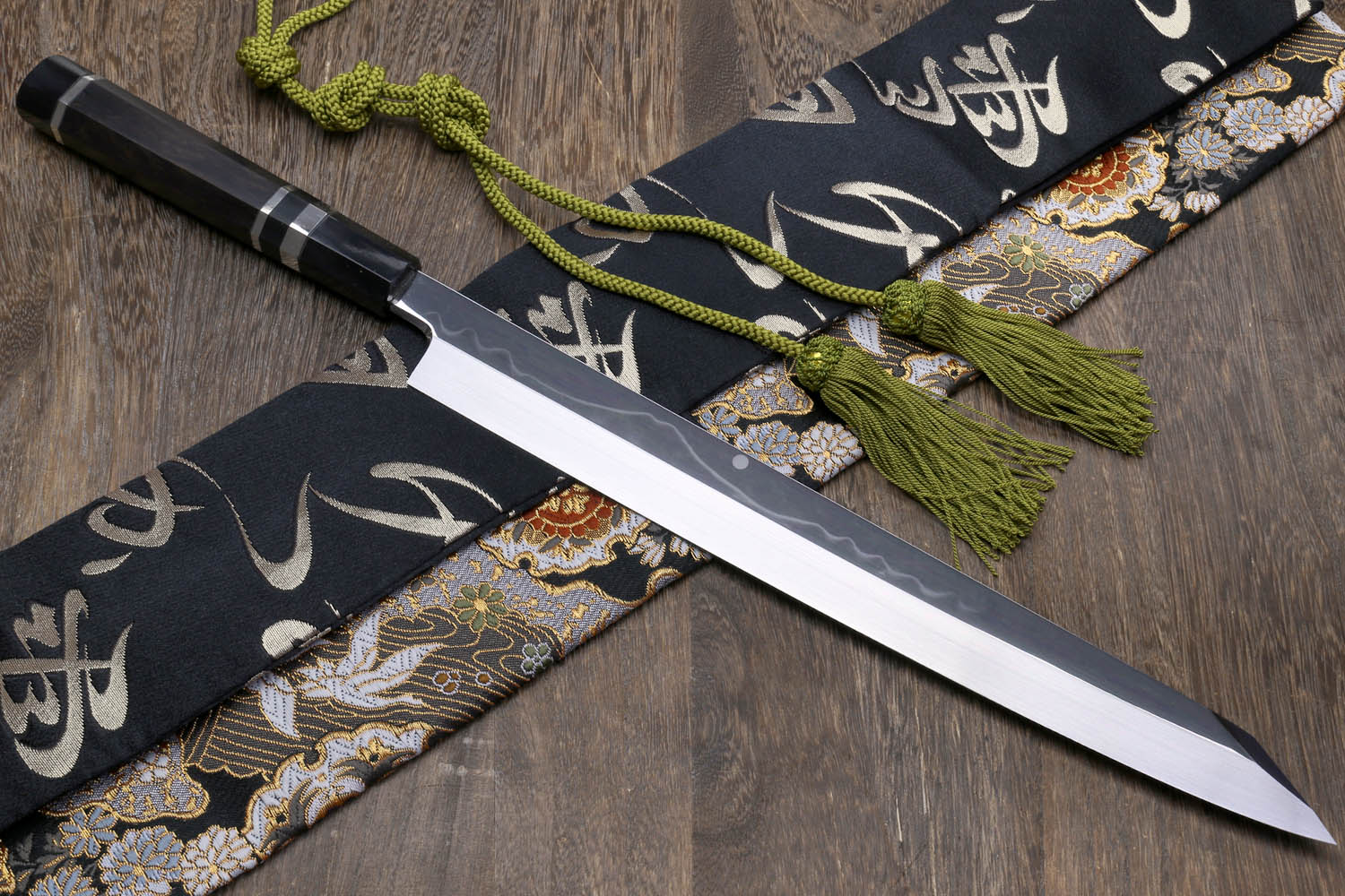 Japanese kiritsuke knife with mirror-finished blade, dark handle, and green tassel cords