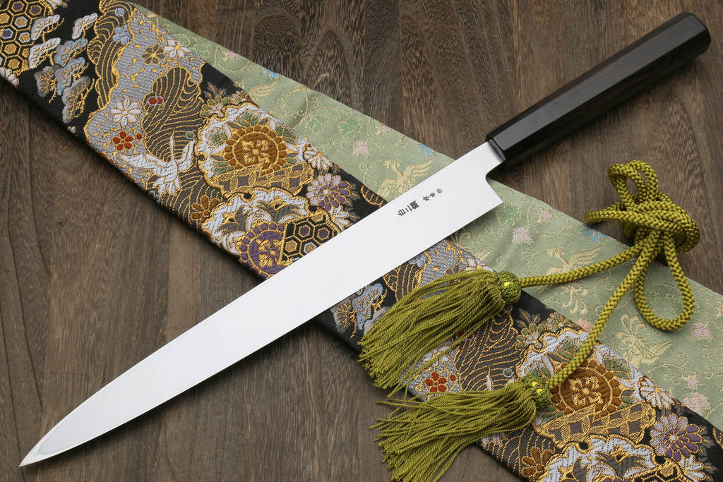 Japanese kitchen knife with mirror blade and black handle, ornate pouch and green tassel ties
