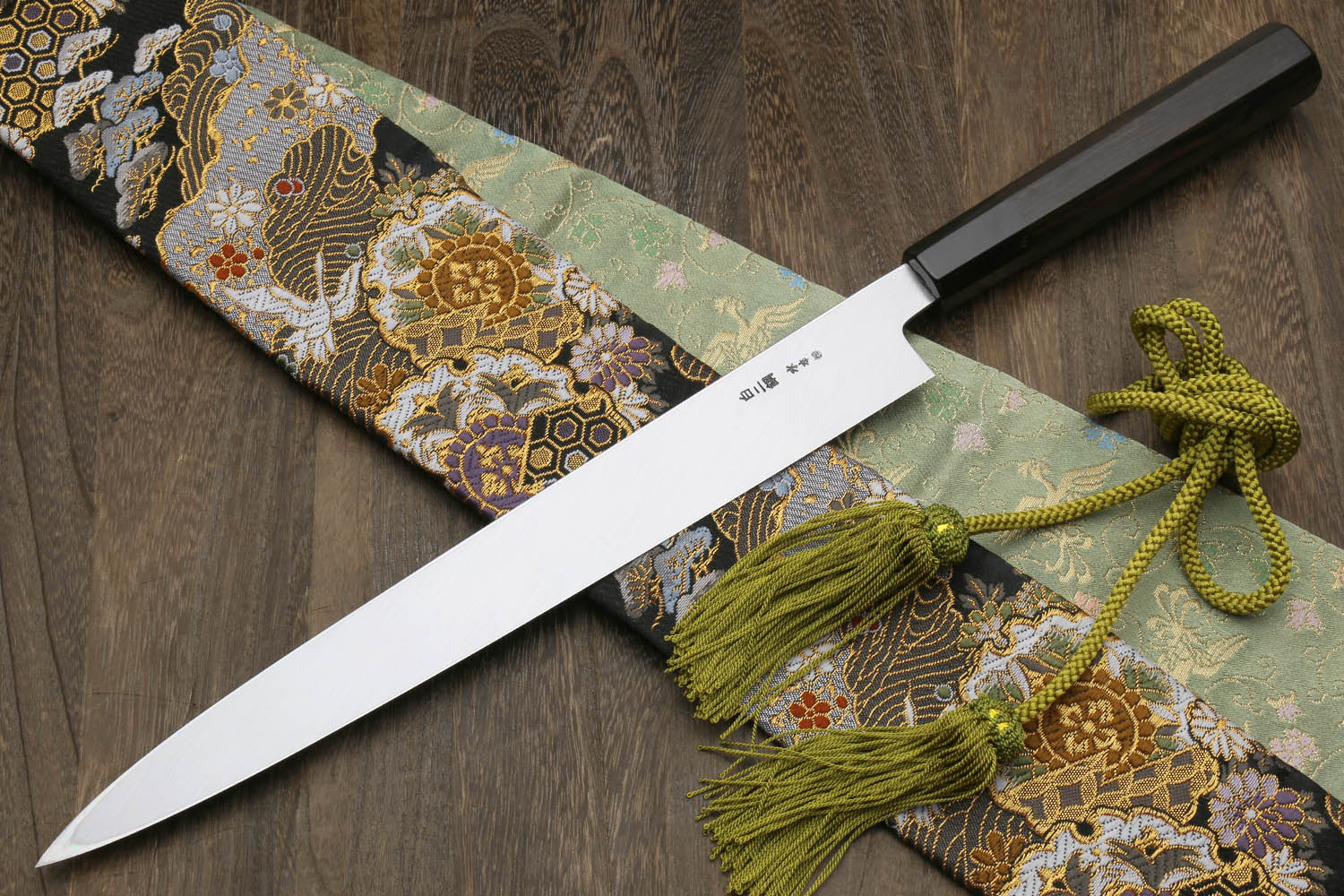 Japanese kitchen knife with mirror blade and black handle, ornate pouch and green tassel ties