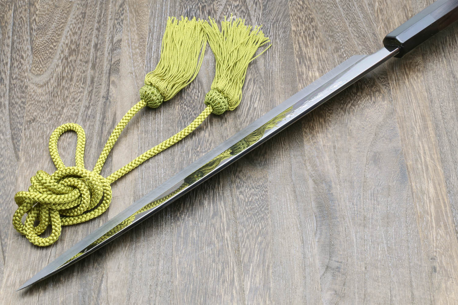 Japanese kitchen knife with black handle and mirror blade, green tassel and cords on cloth